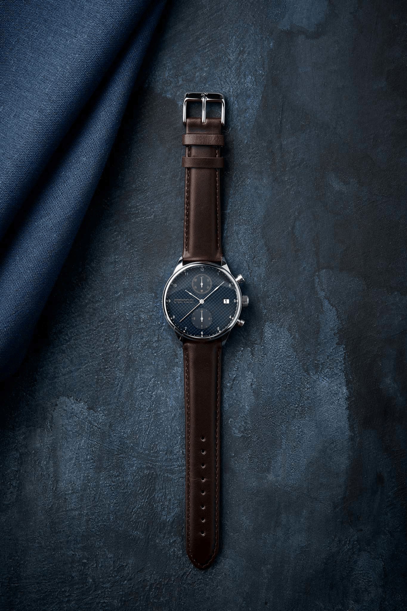 1815 Chronograph by AV86 vintage-inspired chronograph with sapphire crystal, textured dial, and brown leather strap on dark surface