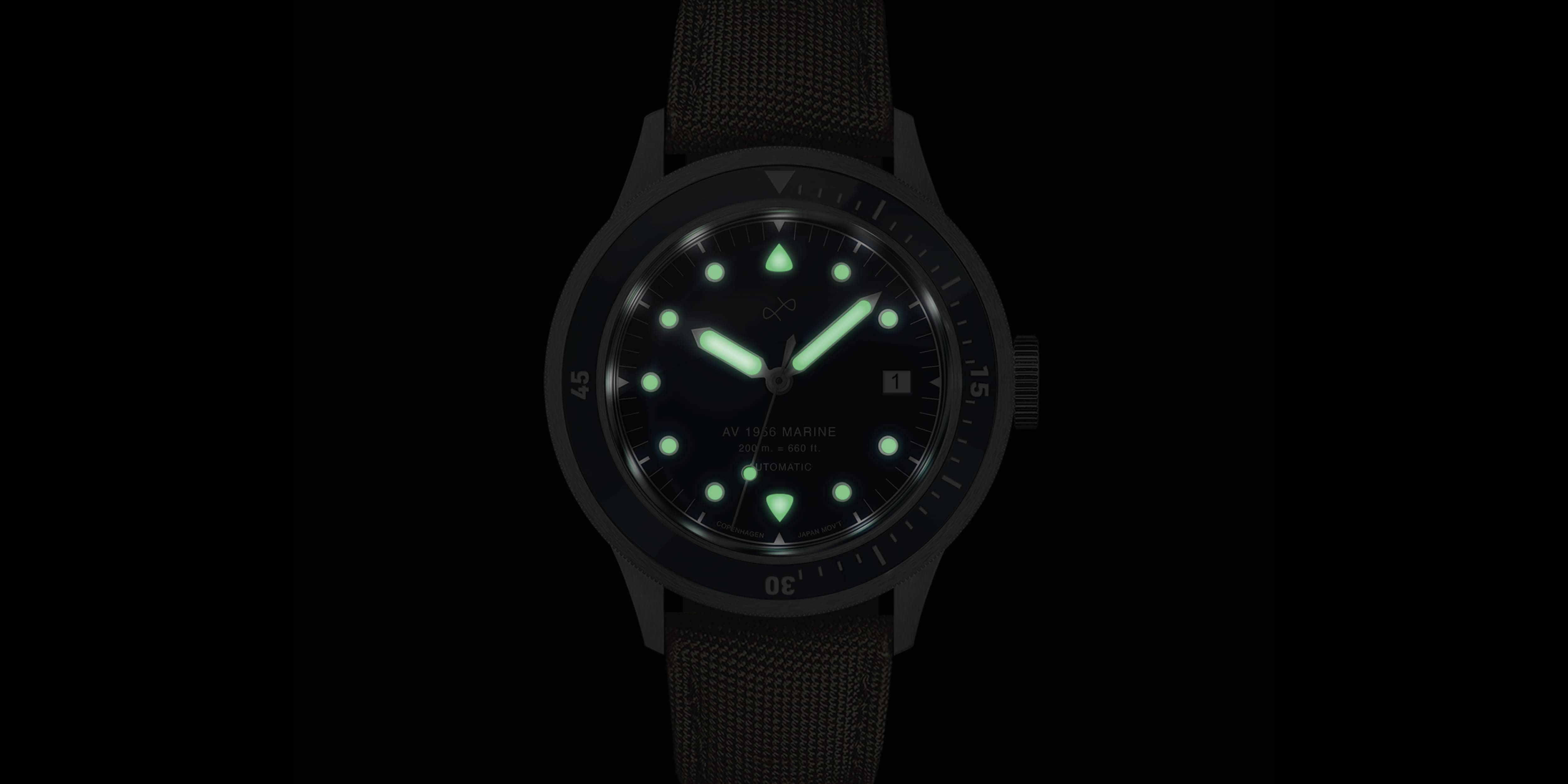 Vintage diver wristwatch glowing with luminescent markers, hands, and bezel on a textured dark brown strap.