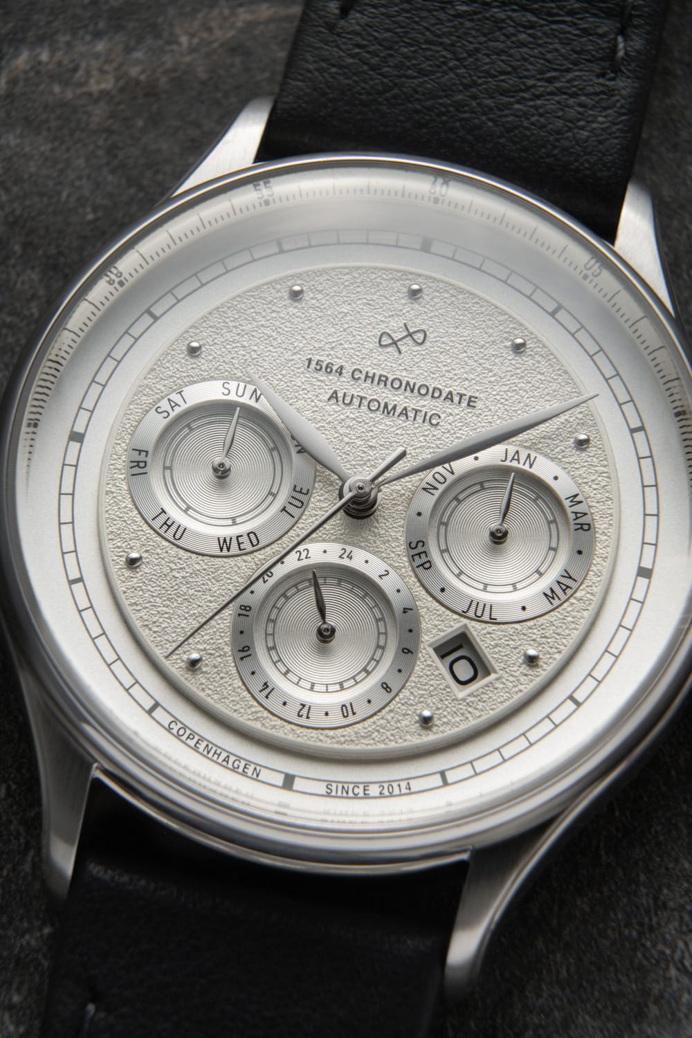 Close-up of an AV86 1564 Chronodate Automatic featuring a textured dial with three subdials displaying day, month, and 24-hour time, a date window, polished case, and a black leather strap, embodying refined Danish design and horological precision.