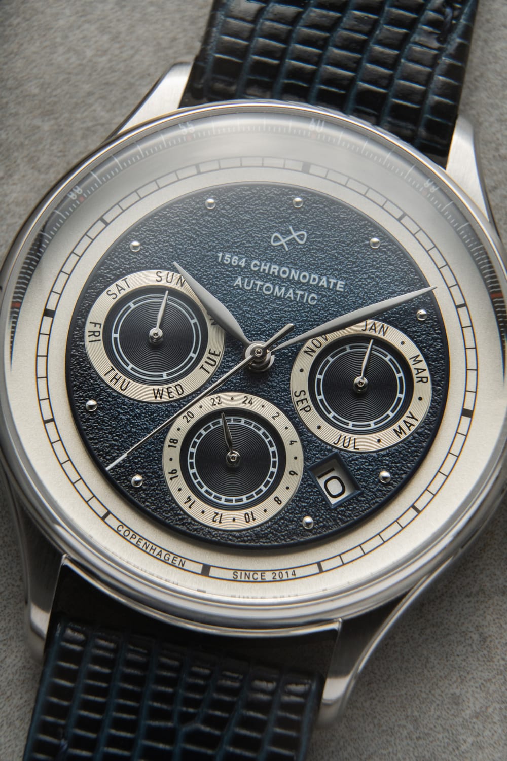 Automatic chronograph watch by AV86 featuring a textured dial with subdials for day, month, and 24-hour time, a date window, and a textured leather strap, reflecting Danish minimalism and horological expertise.