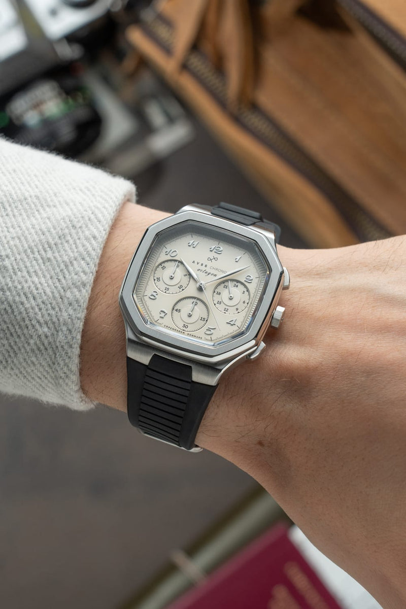 Wrist wearing the 1904 Chrono by AV86, a luxury chronograph with vintage-inspired off white dial, hexagonal steel case, and black textured rubber strap, capturing Nordic minimalism in a casual setting.