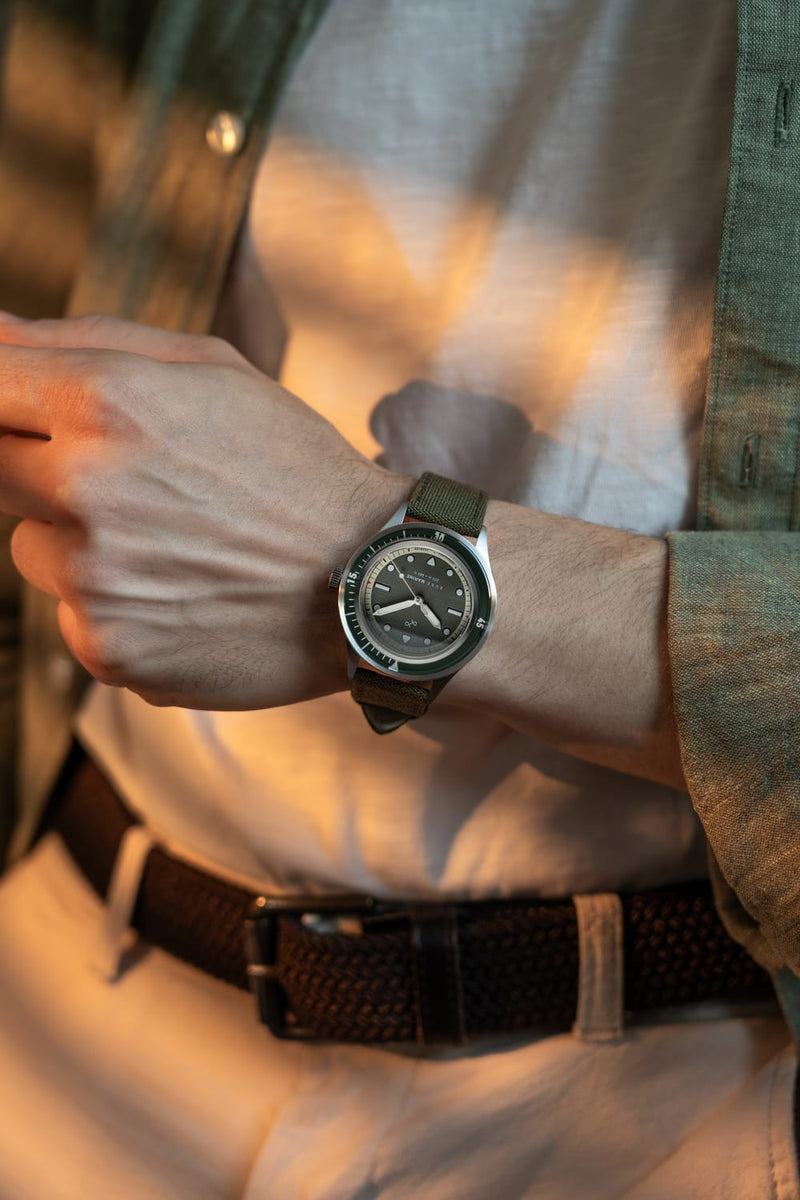 1956 Marine by AV86 vintage-inspired diver with sapphire crystal, compass bezel, and green fabric strap on wrist in casual attire