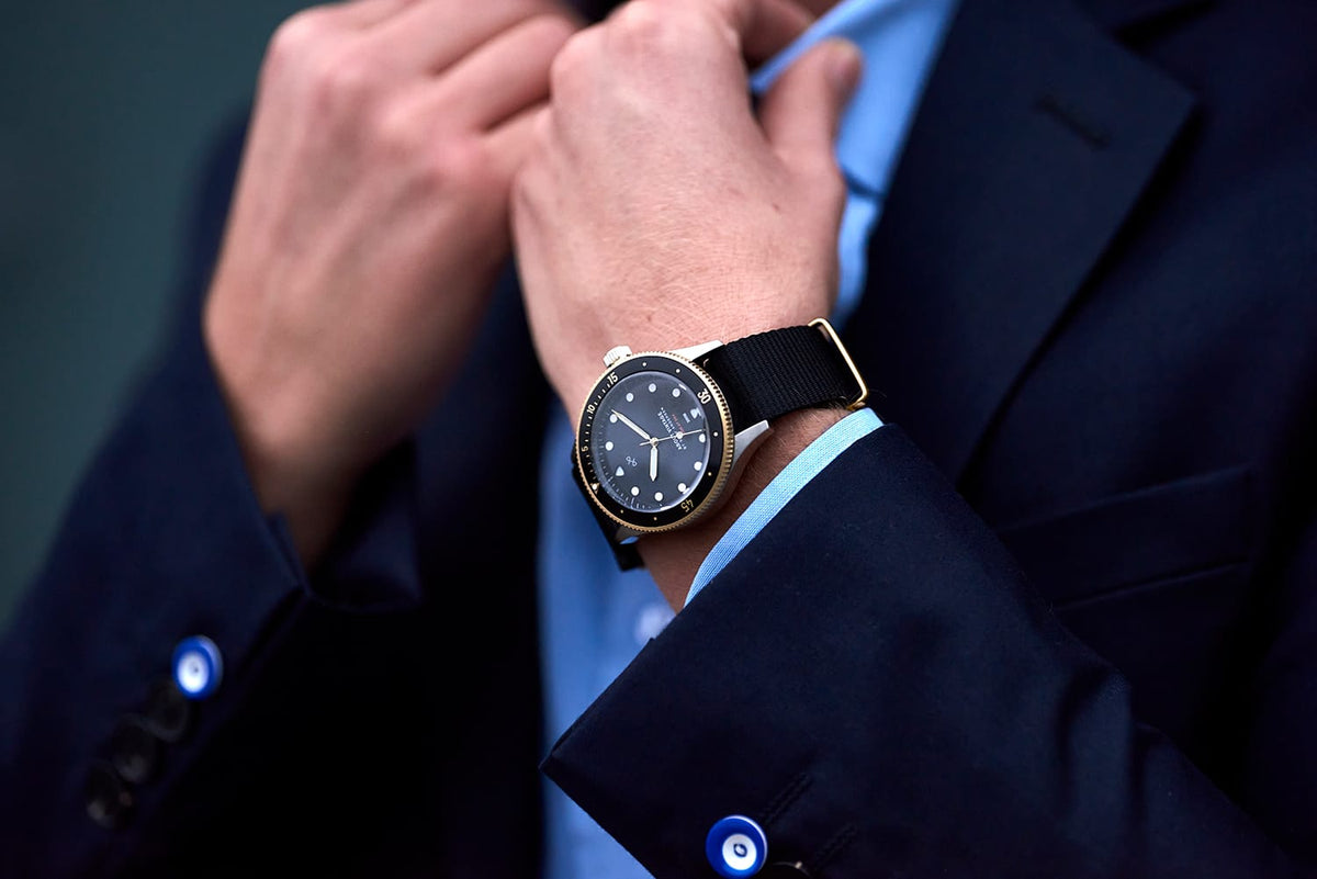 AV86 vintage-inspired dress watch with dark dial and black leather strap worn with a navy suit as a man adjusts his tie
