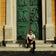 Man dressed in minimalist attire seated against ornate classical door, exuding relaxed Mediterranean style and timeless elegance wearing 1954 Amalfi Mechanical, Gold / Midnight Blue by AV86