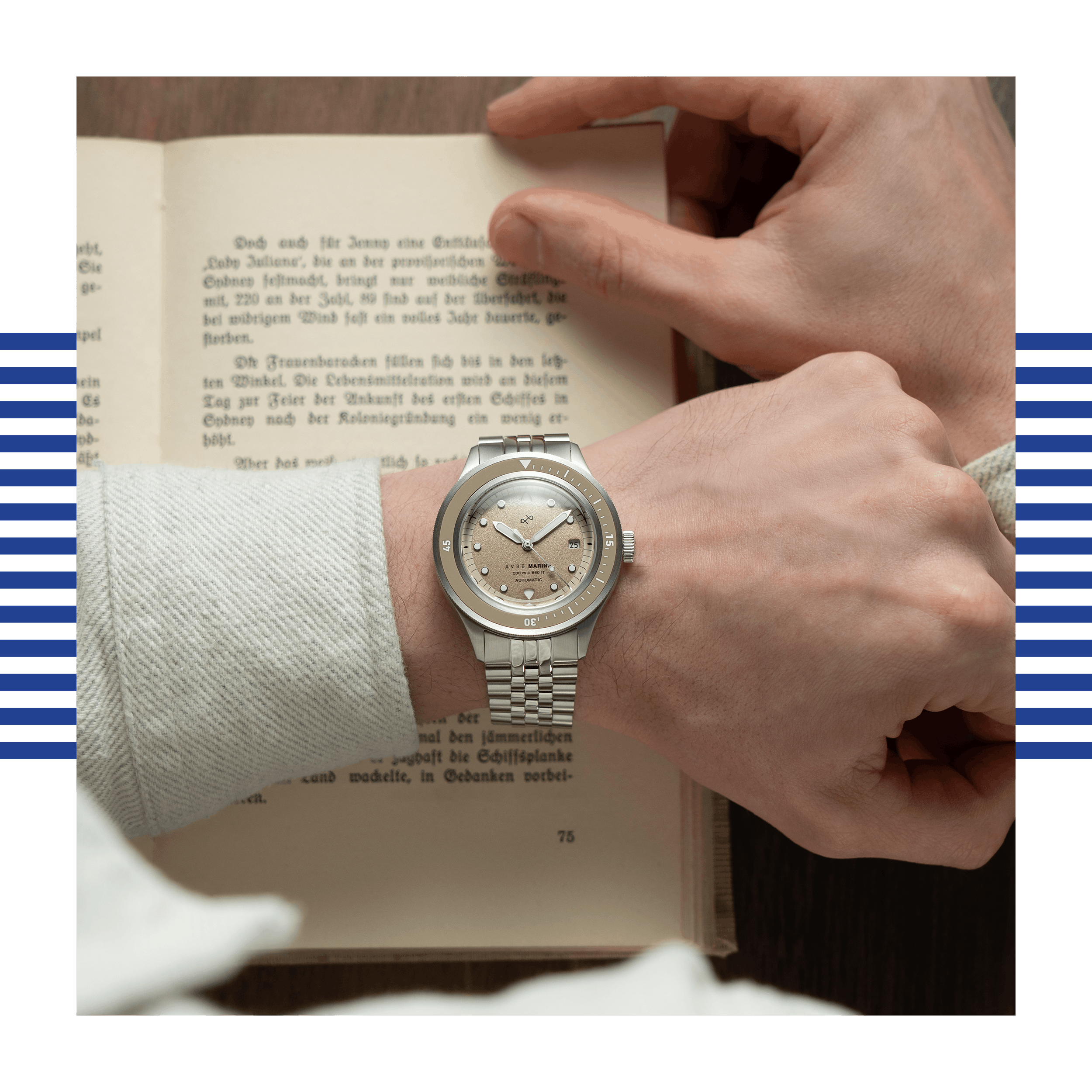 Wrist adorned with a steel watch featuring a sand-colored dial and matching bezel, resting over an open vintage book.