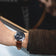 1960 Racing Chronograph by AV86 with vintage-inspired dial, sapphire crystal, and brown leather strap on wrist driving a car