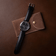1934 Telechron by AV86 features a refined chronograph with a black dial, dual subdials, date window, polished steel case, sapphire crystal, and a smooth black leather strap resting on a brown suede pouch, embodying Danish design and Nordic minimalism.