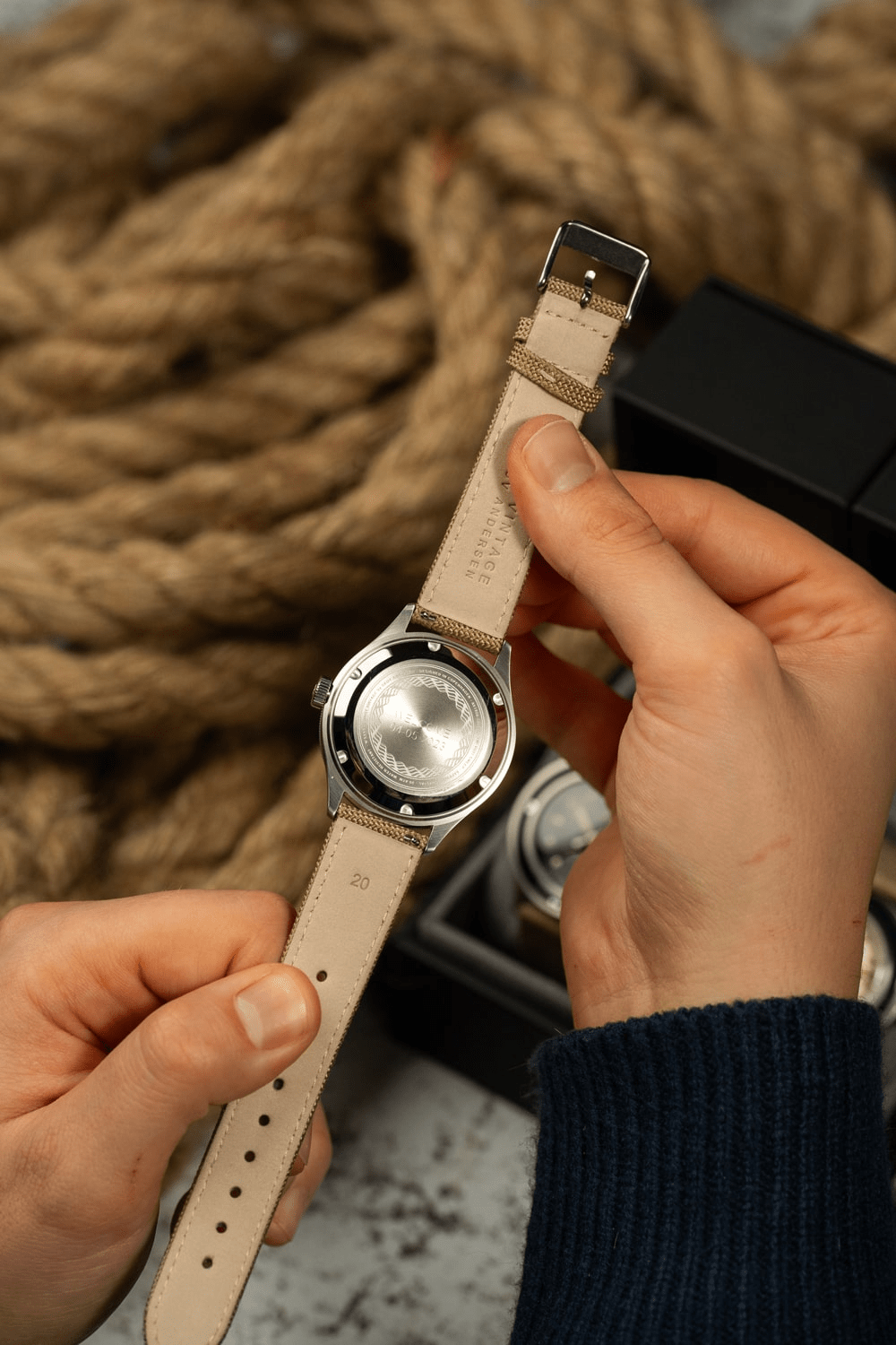 1956 Marine by AV86 showing stainless steel case back and natural leather strap in warm ambient setting with nautical rope background