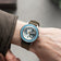 Earthrise WWF Partnership, Automatic / 2026 Edition by AV86 on wrist with a green fabric strap and blue bezel luxury timepiece.