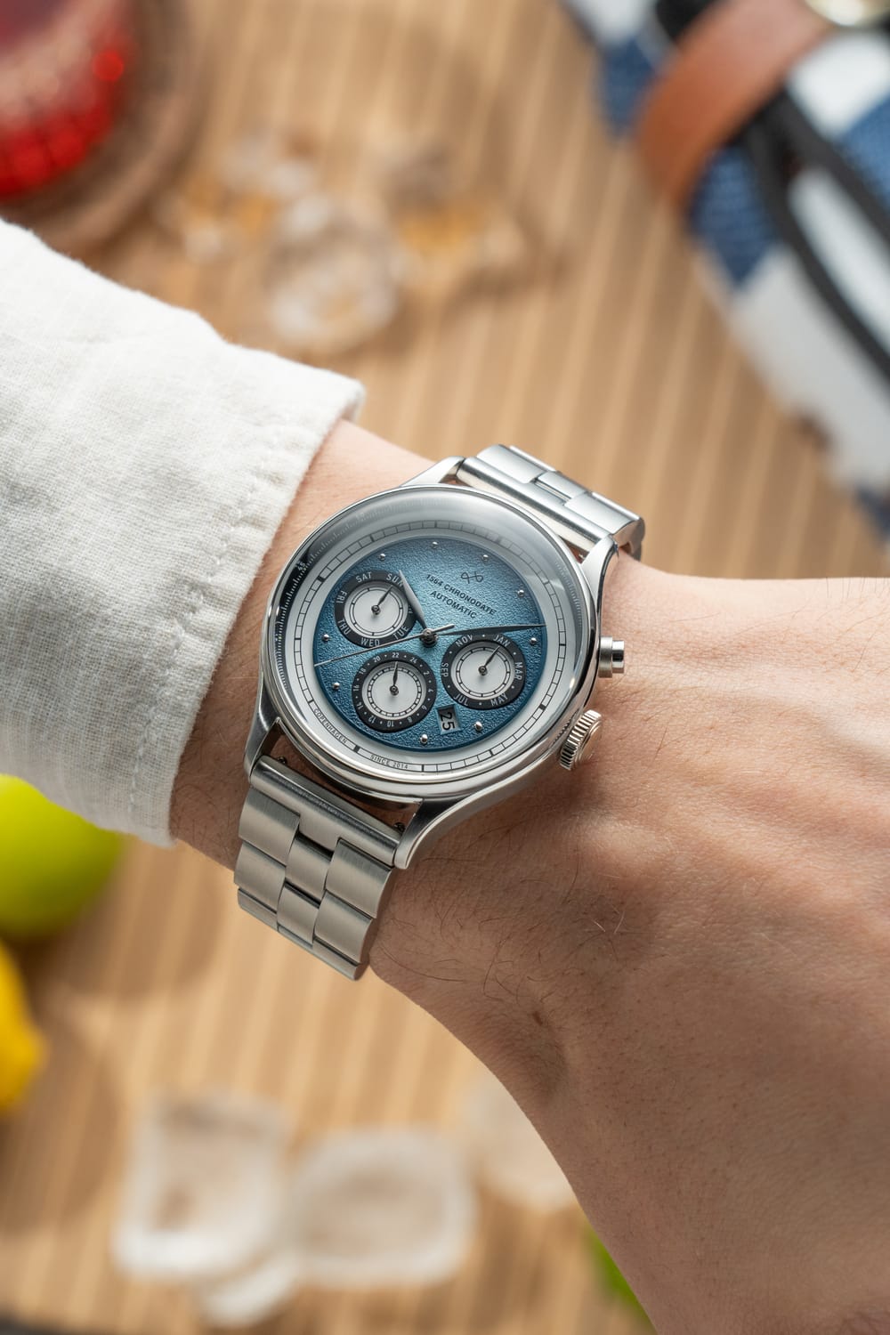 1564 Chronodate Automatic by AV86 featuring a textured ice blue dial with chronograph subdials, polished steel bracelet, and a sophisticated Scandinavian design on a wrist in a casual setting.