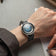 1956 Marine Automatic, Steel / Blue Fade wristwatch by AV86 with a blue fade dial and black leather strap on a wrist writing notes