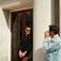 Two men interact beside a sunlit classical building entrance, one wearing sunglasses and a black sweater showcasing the 1564 Chronodate Automatic by AV86, while the other photographs, capturing a moment of casual elegance and Nordic minimalism.
