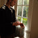 A man stands by a sunlit window adjusting a 1564 Chronodate Automatic, Steel / White on his wrist, dressed in a dark sweater, evoking a calm, refined Nordic ambiance with natural light highlighting the minimalist interior.