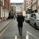A man wearing sunglasses and a tailored dark coat walks confidently down a city street, his 1564 Chronodate Automatic, Steel / Blue by AV86 subtly visible, embodying understated Scandinavian elegance and urban sophistication.