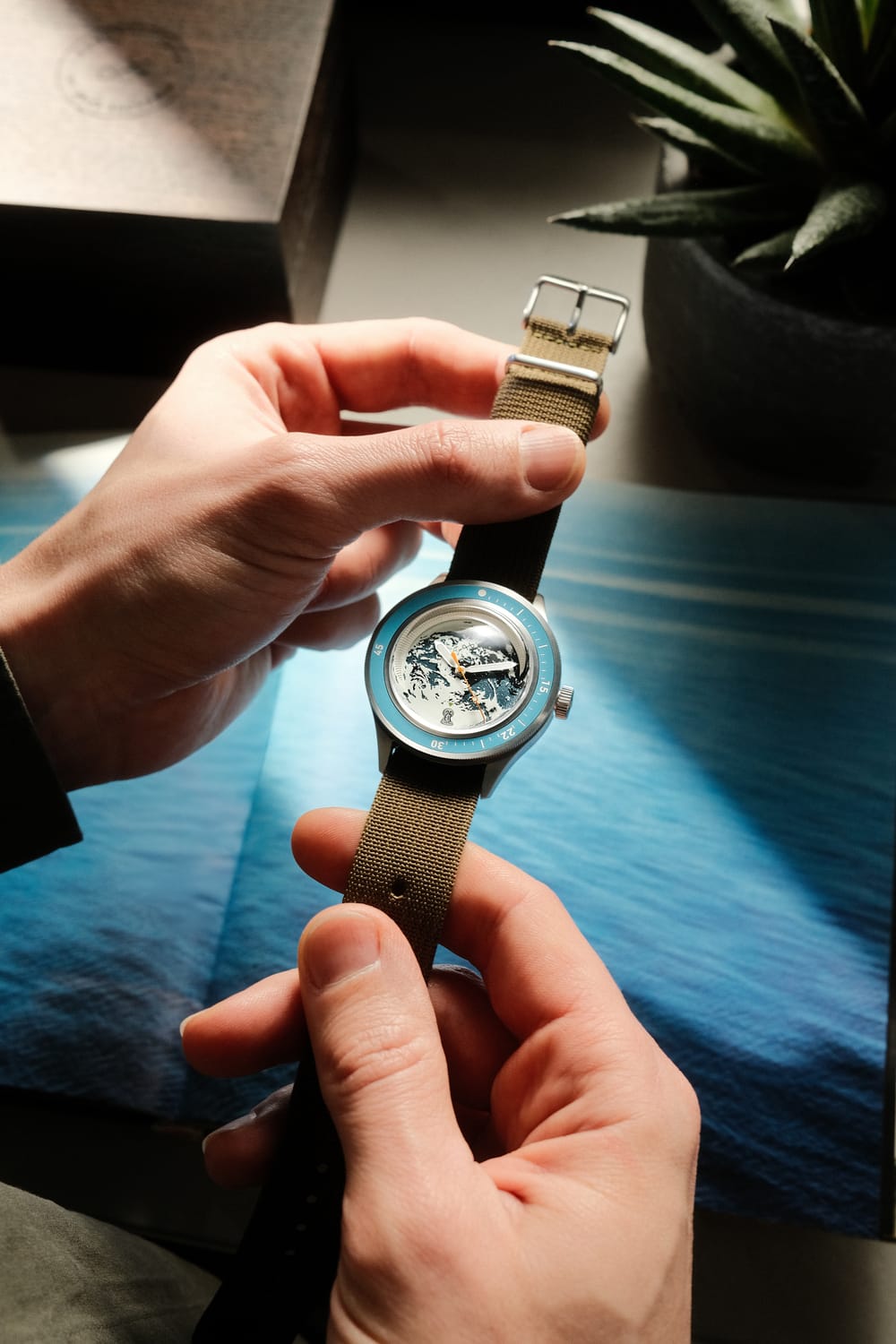 Hands holding Earthrise WWF Partnership, Automatic / 2026 Edition watch by AV86 with fabric strap, textured dial, and blue bezel.