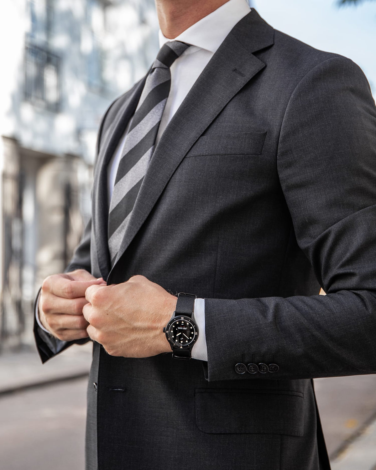 AV86 vintage-inspired chronograph with dark dial and leather strap worn by a suited man fastening his jacket on a city street