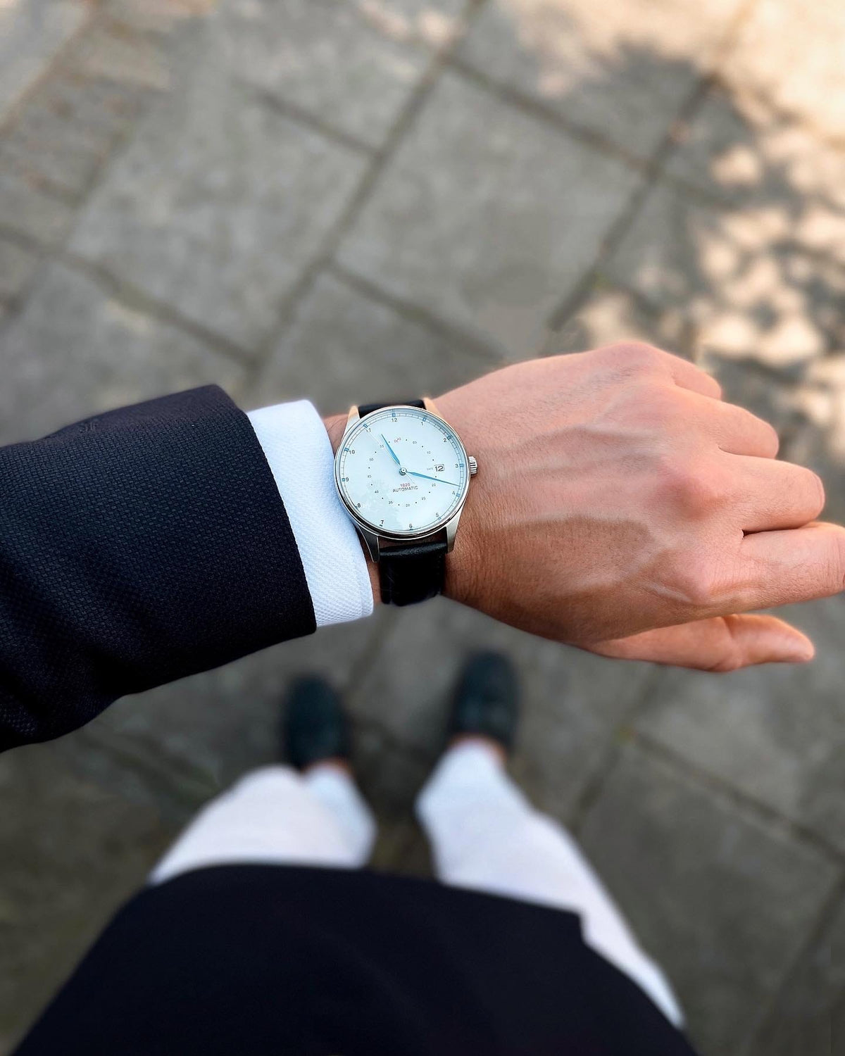 AV86 vintage-inspired dress watch with pale dial and black leather strap worn with a tailored suit on a city sidewalk